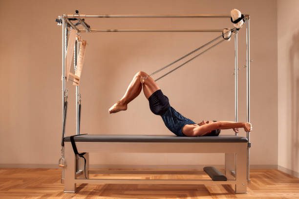 Fit man doing a lunge stretch yoga pilates exercise to strengthen and tone his muscles, using a reformer in a gym in a health and fitness concept.